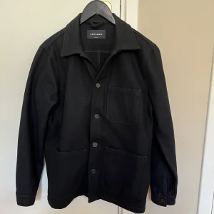 Mötkblå overshirt från A Day's March - Stilren mörkblå overshirt från A Day's March i ullmix. Jackan har tre stora utanpåfickor, klassisk krage och knäppning med fyra knappar framtill. Perfekt lager-på-lager-plagg med rak passform och lång ärm.