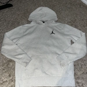 Ljusgrå hoodie från Jordan - Säljer en stilren ljusgrå hoodie från Jordan med klassisk svart Jumpman-logga på bröstet. Tröjan har huva, magficka och långa ärmar. Perfekt för dig som gillar sportig och avslappnad stil.