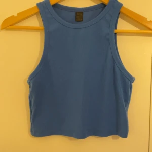 Blå croppad linnetopp - Snygg blå croppad linnetopp med rund halsringning och ärmlös design. Perfekt för varma dagar och enkel att matcha med jeans eller kjol. Mjuk och bekväm känsla tack vare bomullsmaterialet.