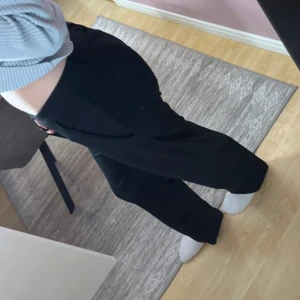 Svarta kostymbyxor med wide fit - Snygga svarta kostymbyxor med låg midja och breda ben. Klassisk design med fickor på sidorna och rak siluett som ger en chill och stilren vibe. Perfekta för dig som gillar en loose och relaxed passform. Materialet känns mjukt och följsamt.