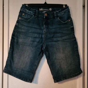Mörkblå denimshorts från LAB industries - Snygga mörkblå jeansshorts med klassisk femficksdesign och knappstängning. Modellen är rak och har en normal passform med medellång längd. Perfekt för dig som gillar en enkel och stilren look.