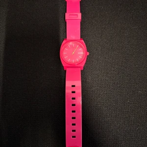Rosa Nixon Time Teller P klocka - Säljer en snygg och färgstark Nixon Time Teller P klocka i helrosa design. Klockan har rund urtavla, minimalistiska vita markeringar och gröna visare. Boetten och armbandet är tillverkade i polykarbonat, vilket gör den lätt och bekväm på handleden.köpt i USA för många år sedan men inte blivit använd så mycket. Nytt batteri behövs! 