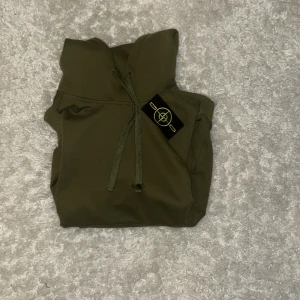 Olivgrön hoodie från Stone Island - Säljer en olivgrön hoodie från Stone Island med klassisk patch på ärmen och justerbar huva med snörning. Tröjan är i mjuk bomull och har en clean look som passar perfekt till streetwear. Snygg och enkel att matcha med jeans eller cargos.