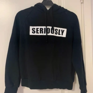 Svart hoodie - Svart hoodie med vit SERIOUSLY-text på bröstet. Tröjan har huva med snörning och långa ärmar