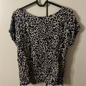 Leopardmönstrad blus från Lindex - Säljer en snygg blus från Lindex med leopardmönster i mörkblått och beige. Blusen har korta ärmar och en omlott v-ringning back, som ger en cool och trendig look. Materialet är mjukt och lätt, perfekt för dig som gillar djurmönster.
