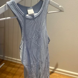 Ljusblå ribbad linnetopp H&M - Säljer en ljusblå ribbad linnetopp från H&M. Toppen är ärmlös med rund halsringning och har en tight passform. Perfekt för varma dagar eller som layering-piece. Materialet är mjukt och stretchigt för extra komfort.