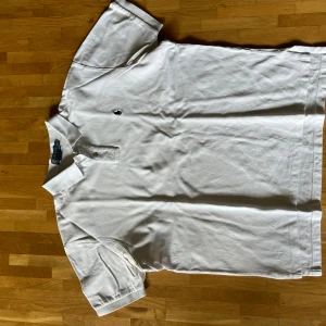 Vit pikétröja från Polo Ralph Lauren XL - Klassisk vit pikétröja från Polo Ralph Lauren i storlek XL. Tröjan har korta ärmar, krage med två knappar och den ikoniska broderade loggan på bröstet. Tillverkad i mjuk bomull som känns skön mot huden.
