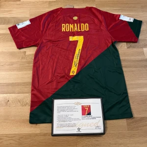 Portugal Ronaldo signerad fotbollströja - Exklusiv Portugal fotbollströja från Nike med Cristiano Ronaldos namn och nummer 7 i gult på ryggen. Tröjan är röd och grön med gul Nike-logga och Portugals landslagsemblem. Kortärmad modell i lätt polyestermaterial. Levereras med äkthetsintyg och Ronaldos autograf på siffran.