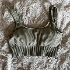 Tränings bh från Aim'n - Säljer en ribbad grön sport bh från Aim'n. Toppen har ett metallmärke med Aim'n-logga framtill och är tillverkad i mjukt, stretchigt material som sitter skönt mot kroppen. Perfekt för gymmet eller annan sport. Köpt på Sellpy för 90kr.