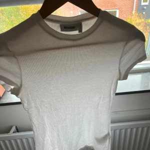 Vit ribbad t-shirt från Weekday - Säljer en vit ribbad t-shirt från Weekday med rund hals och korta ärmar. T-shirten är gjord i mjuk bomull och har en slim passform som sitter snyggt mot kroppen. Perfekt att styla med jeans eller kjol för en clean look.