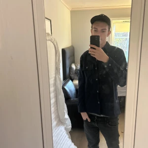 Mörkblå overshirt med knappar - Säljer en stilren mörkblå overshirt med klassisk krage och knäppning framtill. Jackan har två bröstfickor med lock och knappar, samt långa ärmar. Perfekt för lager-på-lager och enkel att matcha med jeans eller chinos.