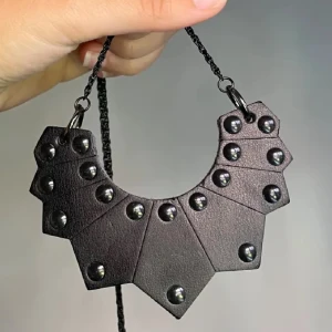 Svart statement-halsband med nitar - Unikt svart halsband i geometrisk form med coola nitar. Halsbandet har en bred, kantig design och är gjort i ett material som liknar skinn. Perfekt för dig som vill sticka ut med en edgy accessoar.