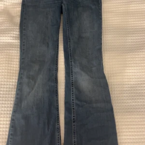 Blå bootcut jeans från Nelly, EU 34 - Snygga blå bootcut jeans från Nelly i storlek EU 34. Jeansen har låg midja och klassisk femficksdesign med dekorativa sömmar på bakfickorna. Materialet är jeans med en mjuk tvättad finish som ger en cool vibe.