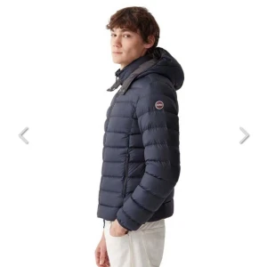 Mörkblå dunjacka från Colmar - Snygg mörkblå dunjacka från Colmar med huva och diskret logga på ärmen. Jackan har quiltad design, dragkedja framtill och hög krage. Perfekt för kyliga dagar och ger en clean look till din outfit. Nypris 4700kr! Mitt pris 3500