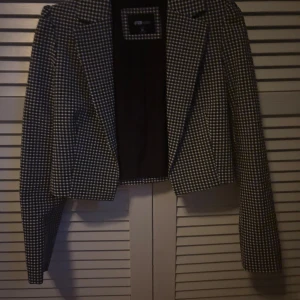 Rutig svartvit kavaj från FB sister - Snygg svartvit rutig kavaj från FBsistee med klassisk krage och lång ärm. Modellen är croppad och har en figurnära passform. Perfekt för dig som vill ha en stilren och trendig look med lite edge.