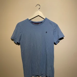 Ljusblå t-shirt från Morris - Snygg ljusblå t-shirt från Morris med diskret logga broderad på bröstet. Klassisk rund hals och korta ärmar. Mjuk bomullskvalitet som känns skön mot huden. Perfekt för dig som gillar stilrena och enkla plagg med en touch av premium.