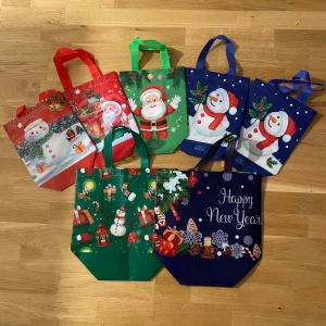 7 Juliga shoppingväskor med snögubbar & tomtar - Flera färgglada shoppingväskor med julmotiv, snögubbar, tomtar och presenter. Väskorna har handtag i rött, grönt och blått och är tillverkade i syntetmaterial. Perfekt för att sprida julstämning när du handlar eller ger bort presenter. Motiv med Happy New Year och klassiska juldetaljer. De stora kostar 20kr styck och de små kostar 10kr styck 