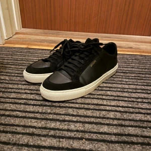 Axel Arigato 90 Triple - Snygga svarta sneakers från Axel Arigato med vit platt sula och diskret guldfärgad logga på sidan. Skorna har rund tå, snörning och är tillverkade i skinn med detaljer i mocka. Perfekt för dig som gillar stilrena och minimalistiska sneakers. Dessa är i väldigt bra skick och sparsamt använda. Nypris: 2750 kr. Köpta på NK