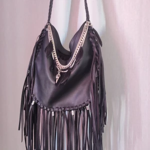 Svart axelväska med fransar och kedjor - Svart, egendesignad fransväska.  Mått: 24 cm hög, 32 cm bred. 9 cm bred botten. 92 cm axelband.  Stängs med dragkedja. 3 mindre fack inuti väskan.  Stor och rejäl med andra ord!  Rymmer 2 långburkar och 5 småburkar, för referens..  Nyskick.  Köp på en gång. Du kommer vara ensam om denna väska då den är den enda i sitt slag.