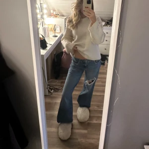 Blå bootcut jeans med hål - Säljer ett par blå jeans med bootcut passform och ett stort hål på ena knät. Jeansen har låg midja och klassisk femficksdesign. Perfekta för dig som gillar en avslappnad och trendig stil.