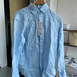 Ljusblå linneskjorta - Ljusblå linneskjorta från Uniqlo, inköpt i somras och är oanvänd som du ser med lappen kvar. Perfekt för en varm sommardag när du behöver någonting luftigare. Storlek xs (normal i storleken), hör av dig vid frågor!