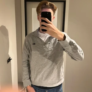 Grå Lexington half zip sweatshirt - Grå sweatshirt från Lexington med half zip och liten broderad logga på bröstet. Tröjan har en hög krage, långa ärmar och är tillverkad i mjuk bomullsmix. Perfekt för chill dagar och enkel att matcha med jeans. Säljer tröjan då den är för liten på mig och kan ha bättre användning hos någon annan.