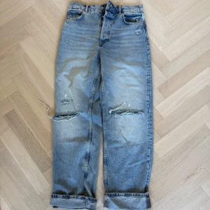 Ljusblå slitna Zara - Ljusblå Zara jeans med raka ben, klassisk femficksmodell och slitna detaljer vid knäna. Jeansen har hög midja, synliga revor och uppvikta benslut för en avslappnad look. Tillverkade i robust denim av bomull.