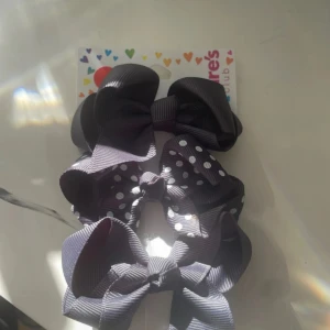 Svarta diademrosetter från Claire's - Tre snygga svarta rosetter på diadem från Claire's, varav en har coola vita prickar. Rosetterna är breda och gjorda i ett syntetmaterial med lätt glans. Perfekt för att ge din look en extra touch med en stor rosett i håret.