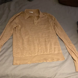 Beige pikétröja med lång ärm, C - Snygg beige pikétröja från C i storlek M. Tröjan har klassisk krage, knäppning med två knappar och långa ärmar. Materialet är mjukt och lätt, perfekt för lager-på-lager. Ribbstickade muddar vid ärmslut och nederkant ger en clean look.