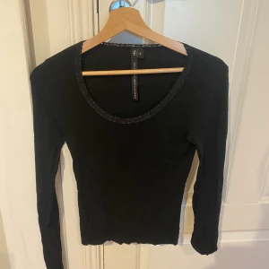 Svart långärmad topp - En svart långärmad topp från Lager 157 med rund halsringning och diskret spetskant. Modellen är slim och passar perfekt till jeans eller kjol. Tunn och mjuk känsla, enkel att styla för olika looks.