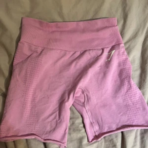 Ljusrosa seamless shorts från Gymshark - Säljer ett par ljusrosa seamless shorts från Gymshark med hög midja och ribbad linning. De har diskreta texturdetaljer längs sidorna och är perfekta för träning. Materialet är mjukt och stretchigt syntet som sitter tight och bekvämt.