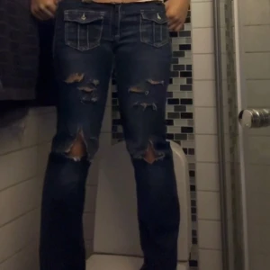 PRIS GÅR ATT DISKUTERAS  - Säljer ett par mörkblå jeans med slitningar och hål på knäna. Jeansen har raka ben och coola fickor med lock framtill. Perfekta för dig som gillar en edgy streetstil.