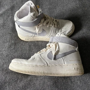 Nike Air Force 1 High x Alyx vita - Exklusiva Nike Air Force 1 High i samarbete med 1017 ALYX 9SM. Skorna är vita med ljusgrå detaljer, tillverkade i premium skinn och har en unik metallspänne vid ankeln. 