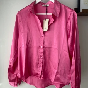 Rosa skjorta i satin från JDY - Säljer denna rosa skjorta från JDY i satinmaterial. Har aldrig använt den, så den är    i princip i ny skick.😊Köpt för 229kr