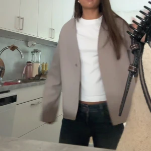 Beige kappa - Stilren beige kavajjacka med rak och oversized passform. Jackan har enkel knäppning framtill och långa ärmar. Perfekt för dig som gillar minimalistisk och clean look. Materialet ser ut att vara i ullblandning för en mjuk känsla.