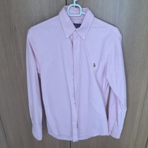 Rosa skjorta från Ralph Lauren S - Säljer en stilren rosa skjorta från Ralph Lauren i slim fit. Skjortan har klassisk krage med knappar, lång ärm och broderad logga på bröstet. Tillverkad i mjuk bomull och passar perfekt för en clean och fräsch look.