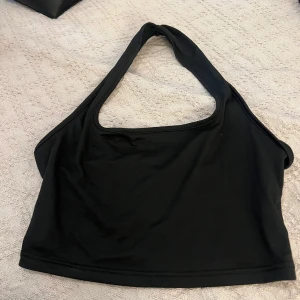 Svart asymmetrisk bikiniöverdel - Snygg svart bikiniöverdel med asymmetrisk design och bred axelrem. Stilren och enkel modell som ger en modern look. Perfekt för strandhäng eller poolparty. Tillverkad i mjukt och stretchigt material för skön passform.