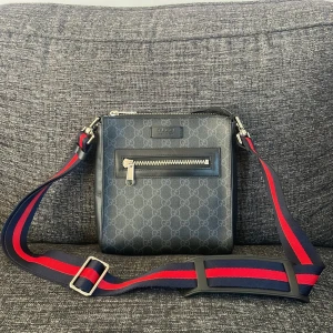 Svart axelväska med mönster - Snygg svart axelväska med ett subtilt mönster och en justerbar axelrem i rött och blått. Väskan har en praktisk dragkedja framtill för enkel åtkomst till dina saker. Nypris 11 000kr! Tveka verkligen inte på att höra av er, otroligt sjukt pris och perfket för att bära med sig det nödvändigaste med stil 👀