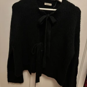 Svart kofta med knyt från Gina tricot - Mysig svart kofta från Gina med knytband både vid halsen och framtill. Koftan är stickad och har lång ärm, perfekt för lager-på-lager. Enkel att styla till olika outfits och superbekväm att bära.