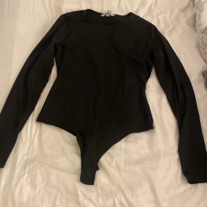 Svart långärmad body från H&M - Svart långärmad body från H&M med rund halsringning. Tight passform som sitter snyggt mot kroppen och ger en clean look. Perfekt att styla med jeans eller kjol för en enkel men stilren outfit.
