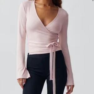Wrap top - Supersöt ljusrosa omlottopp från Gina Tricot med långa ärmar och v-ringning. Toppen har ett knytband i midjan som ger en snygg passform. Perfekt för dig som gillar en feminin och trendig look.