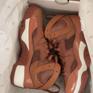 Bruna chunky sneakers med vita detaljer - Säljer ett par riktigt snygga chunky sneakers i brunt med vita detaljer. Skorna har högt skaft, coola paneler i både skinn och mesh samt bred sula. Perfekta för dig som vill sticka ut med en modern och sportig look.