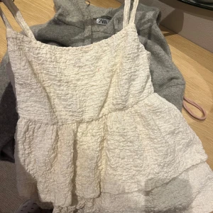 Vit volangtopp från Gina Tricot - Supersöt crémebegia topp från Gina Tricot med tunna axelband och flera lager volanger. Toppen har en krinklad struktur o är i super fint skick💕