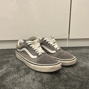 Gråa Vans Old Skool sneakers - Säljer ett par klassiska Vans Old Skool sneakers i grå mocka och canvas med vita detaljer och snörning. Skorna har den ikoniska vita sidoremsan och platt sula, perfekt för en avslappnad streetstil.