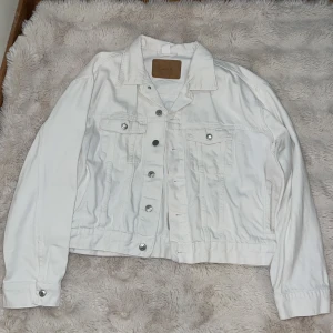 Vit jeansjacka från &Denim, XL - Snygg vit jeansjacka från &Denim i storlek XL. Klassisk modell med silvriga knappar, två bröstfickor med lock och knäppning samt sidofickor. Jackan har krage och långa ärmar med knapp vid ärmslut. Perfekt för dig som vill ha en clean och fräsch look.