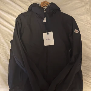 Traversier giubbotto TG3 - Köpte den för 16000kr. Helt oanvänd. Alla original saker finns med förutom påsen. Svart vindjacka från Moncler med minimalistisk design, huva och dragkedja framtill. Jackan har Moncler-logga på ärmen och är tillverkad i lätt polyester. Perfekt för dig som gillar stilrena och funktionella plagg.