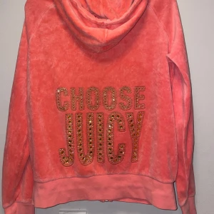 Vintage Juicy Couture rosa hoodie med strass - Superfin rosa hoodie från Juicy Couture i mjuk velour med dragkedja och huva. På ryggen står det 'CHOOSE JUICY' i stora bokstäver dekorerade med glittrande strass. Perfekt statement-plagg för dig som gillar att sticka ut. Priset går att diskutera 
