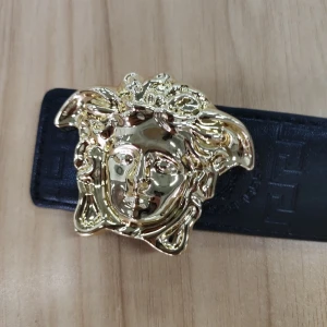 Svart Versace-bälte med Medusa-spänne - Snyggt svart bälte från Versace med ikoniskt guldigt Medusa-huvud som spänne. Bältet är gjort i präglat skinn med diskret mönster längs hela remmen. Perfekt för dig som vill sticka ut med en lyxig detalj i outfiten.