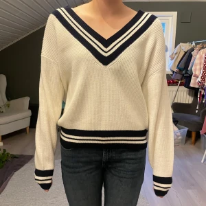 Vit stickad v-ringad tröja med ränder - Vit stickad tröja med mörkblå och vita ränder vid v-ringad hals, ärmslut och midja. Tröjan har en loose passform och långa ärmar. 