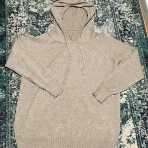 Beige kachmir hoodie med snörning - Mysig beige stickad hoodie med huva och snörning. Tröjan har långa ärmar och ribbade muddar vid ärmslut och nederkant. Perfekt för lager-på-lager och chill dagar. Enkel och stilren design som passar till det mesta.